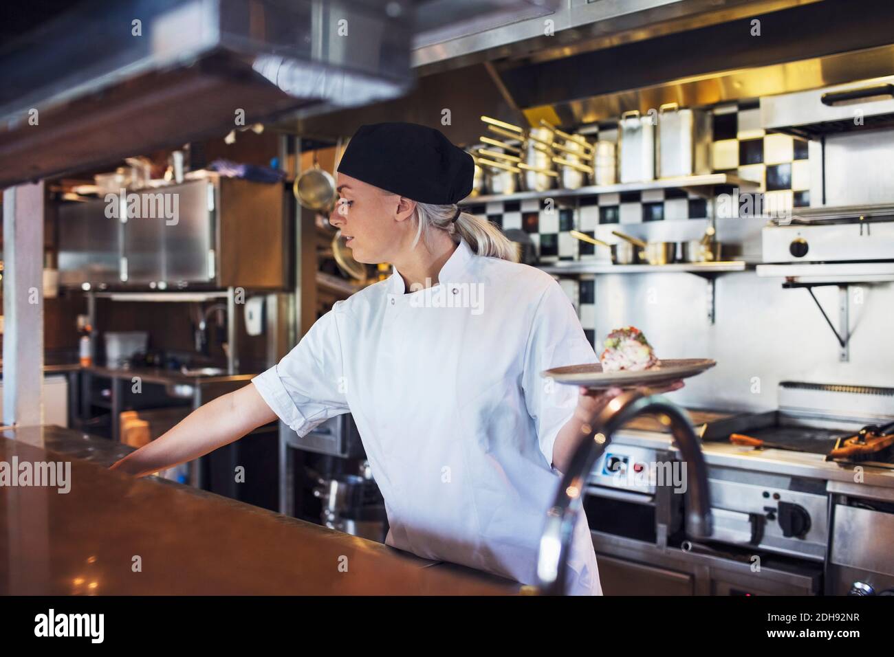 Female chef holding plate in kitchen at restaurant Stock Photo