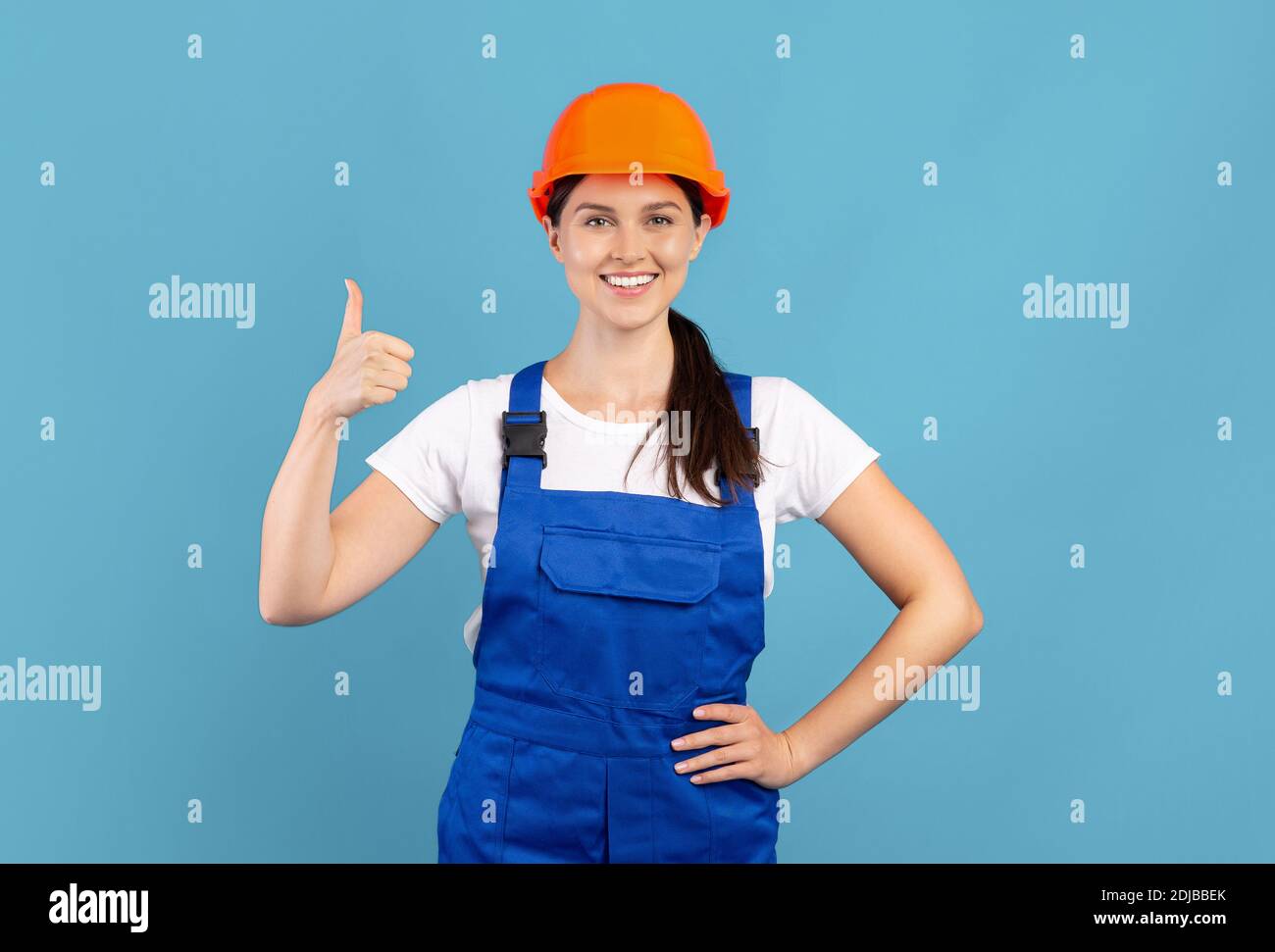 Portrait Of Young Handywoman Lady In Hardhat And Coveralls Showing Thumb Up Stock Photo