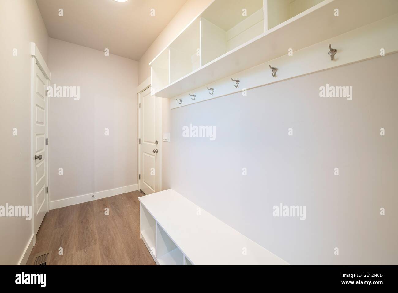 Empty room inside a home with wooden floor built in shelves hooks and two doors Stock Photo