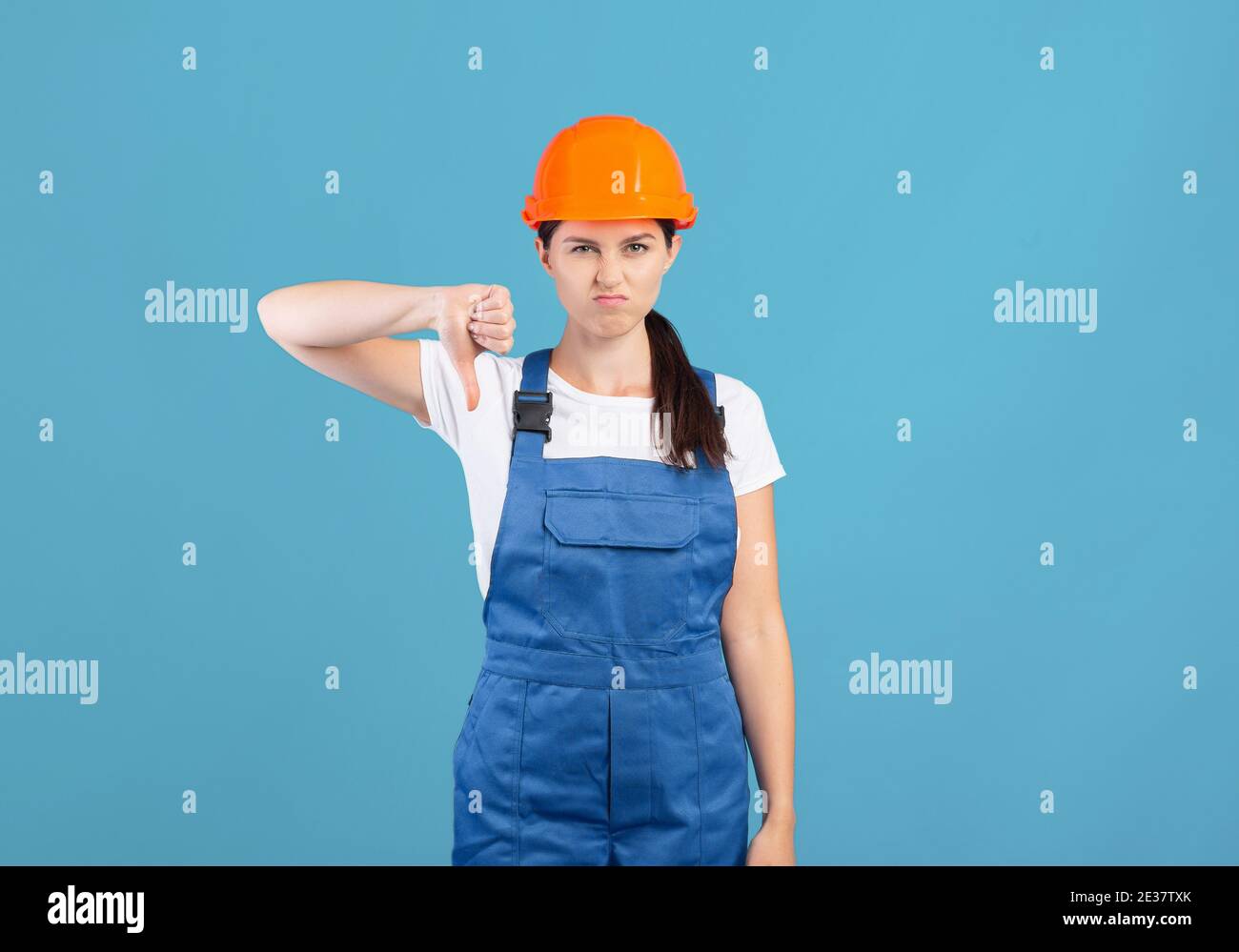 Portrait Of Young Handywoman Lady In Hardhat And Coveralls Showing Thumb Down Stock Photo