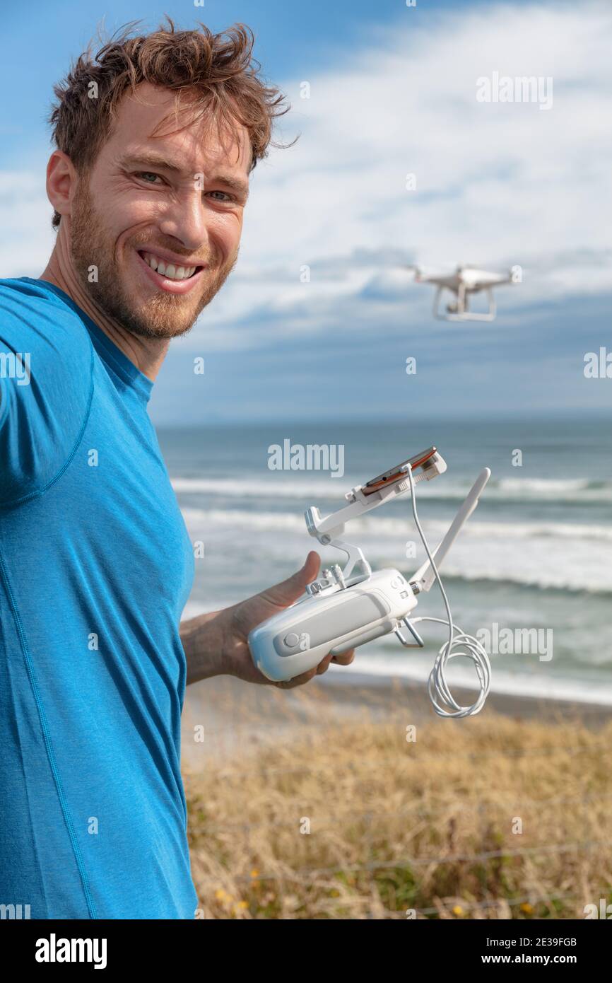 Person flying a drone on beach outdoors gaming young man pilot controlling drong with controller and smart phone taking selfie on travel vacation Stock Photo