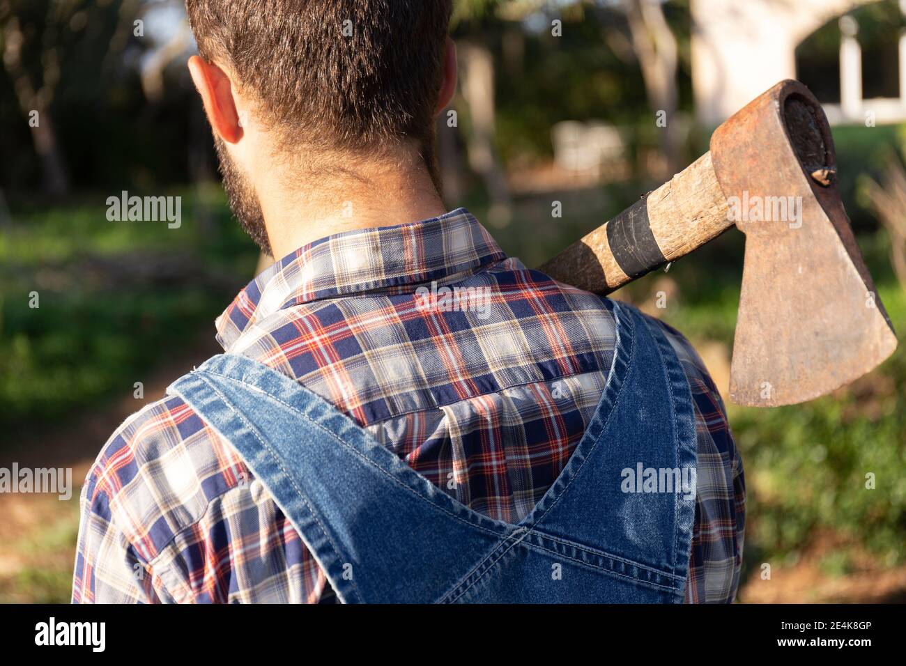 Man in coveralls carrying axe on sunny day Stock Photo