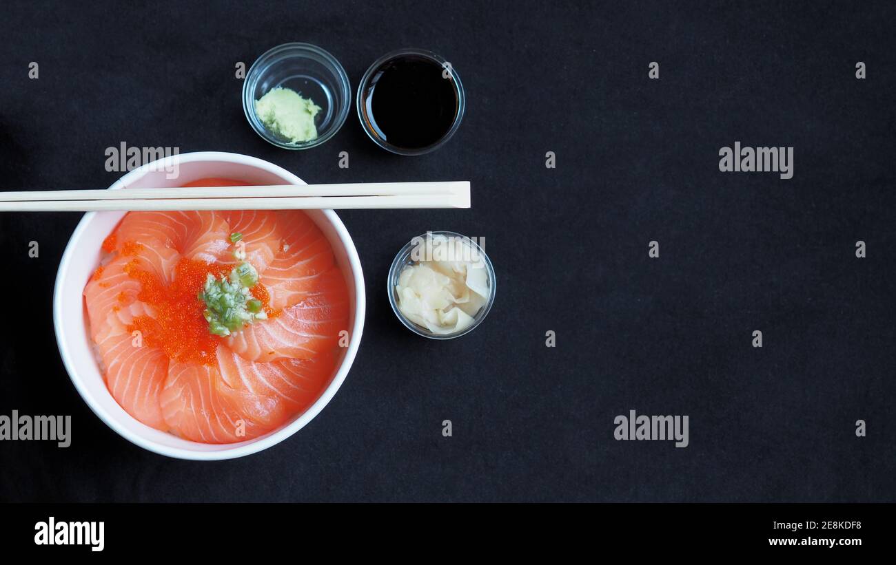 Top view and focus to Salmon with Japanese rice or Salmon Ikura Don in paper dish from delivery restaurant on black Table cloths Stock Photo