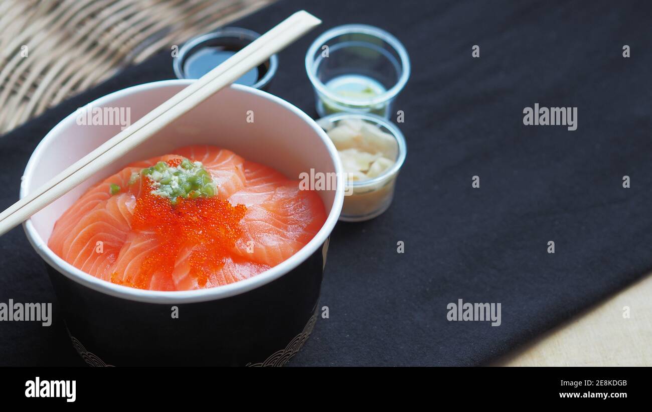 Top view and focus to Salmon with Japanese rice or Salmon Ikura Don in paper dish from delivery restaurant on black Table cloths Stock Photo