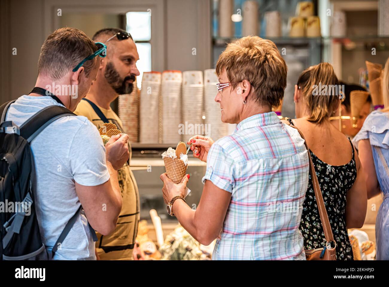 Siena, Italy - August 27, 2018: Two candid people eating ice cream gelato cones with spoons on Italian street in old town village in Tuscany man woman Stock Photo