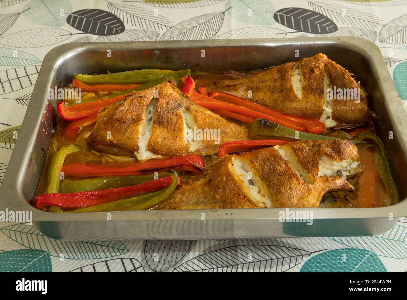 Homemade roasted red fish with red, green peppers and onions ready to eat. Stock Photo