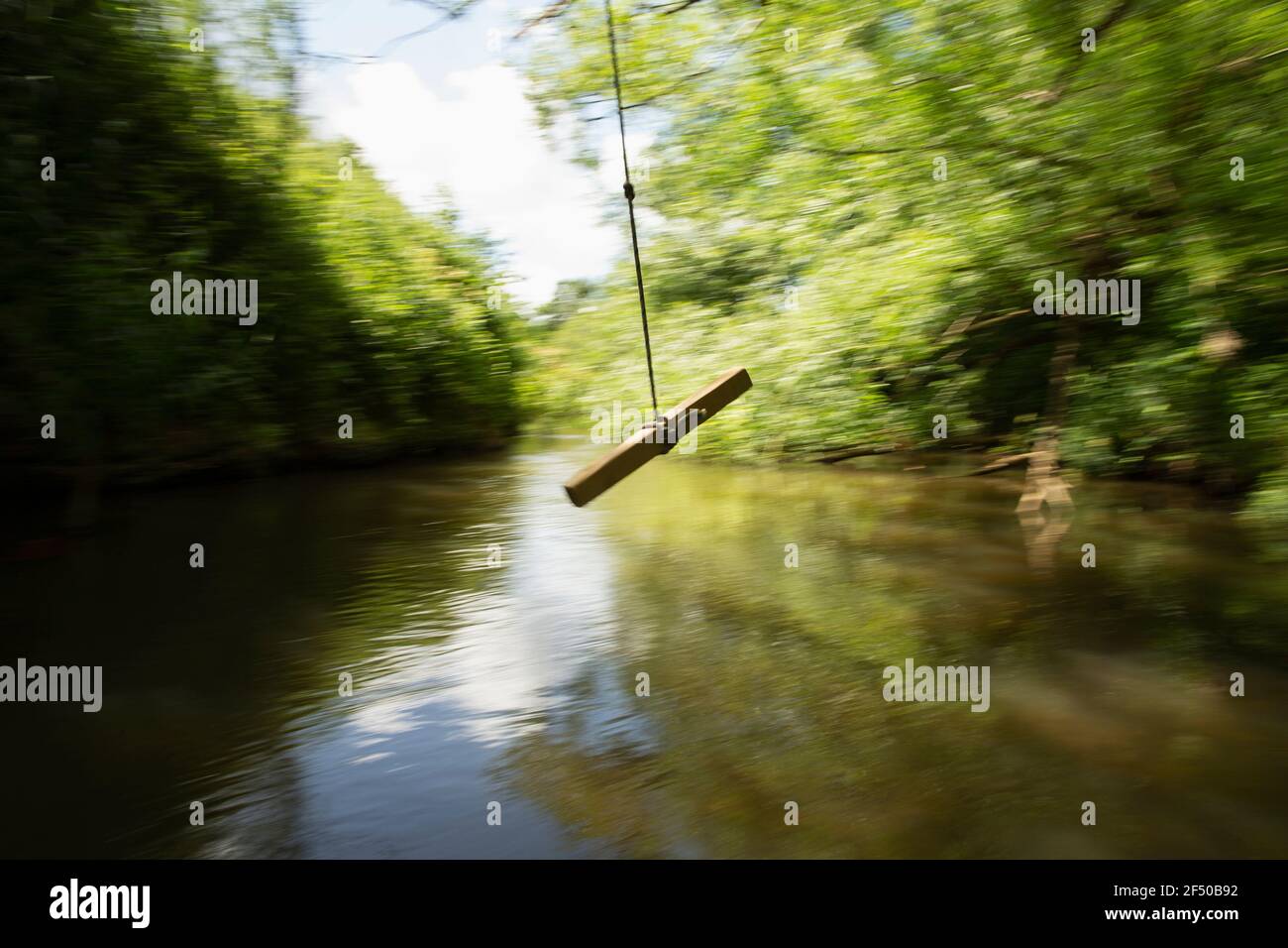 Rope swing swinging above green river Stock Photo