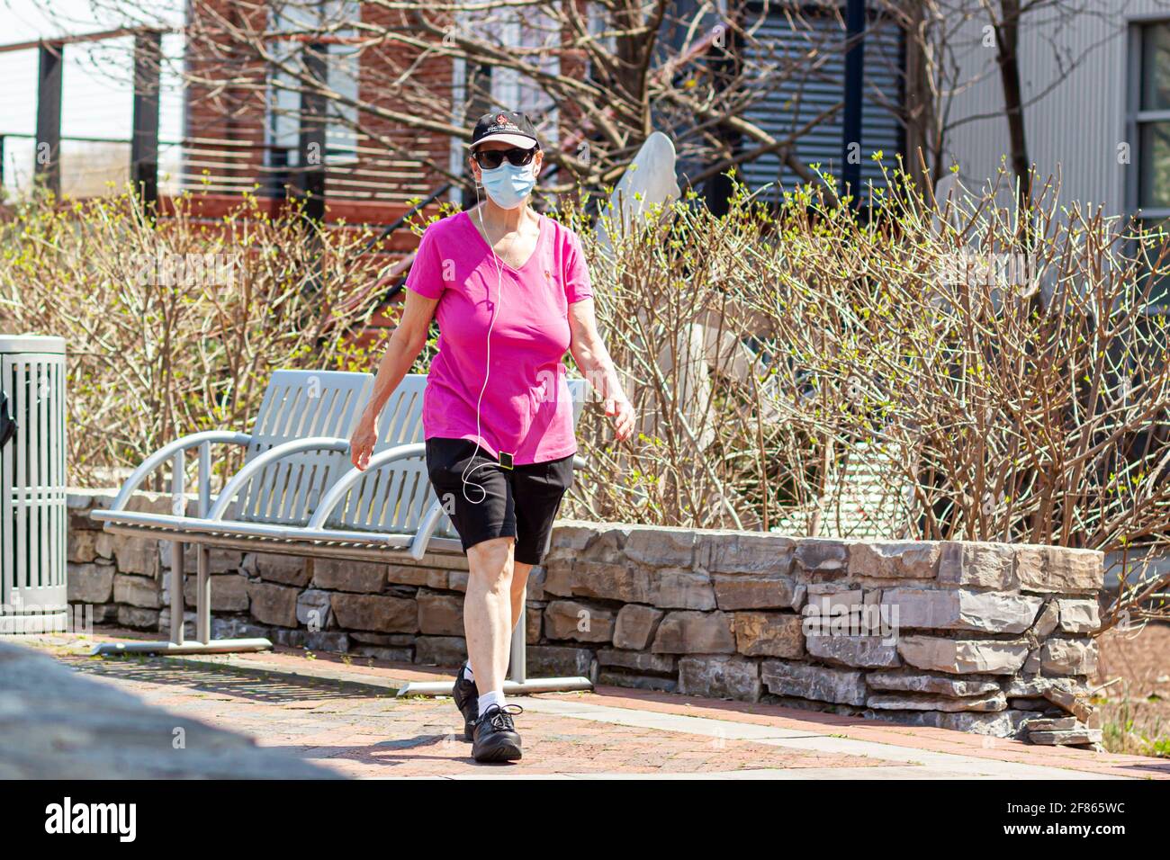 Frederick, MD, USA 04-07-2021: A caucasian middle aged woman wearing shorts, t shirt and sneakers is walking for healthy lifestyle in the park on sunn Stock Photo