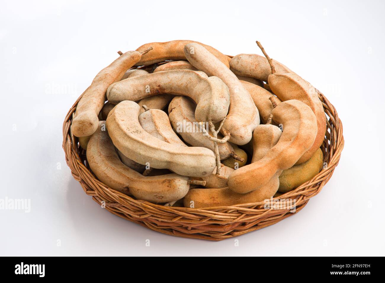 Tamarind_ bean like pods filled with seeds surrounded by a fibrous pulp arranged in a basket with white textured background. Stock Photo