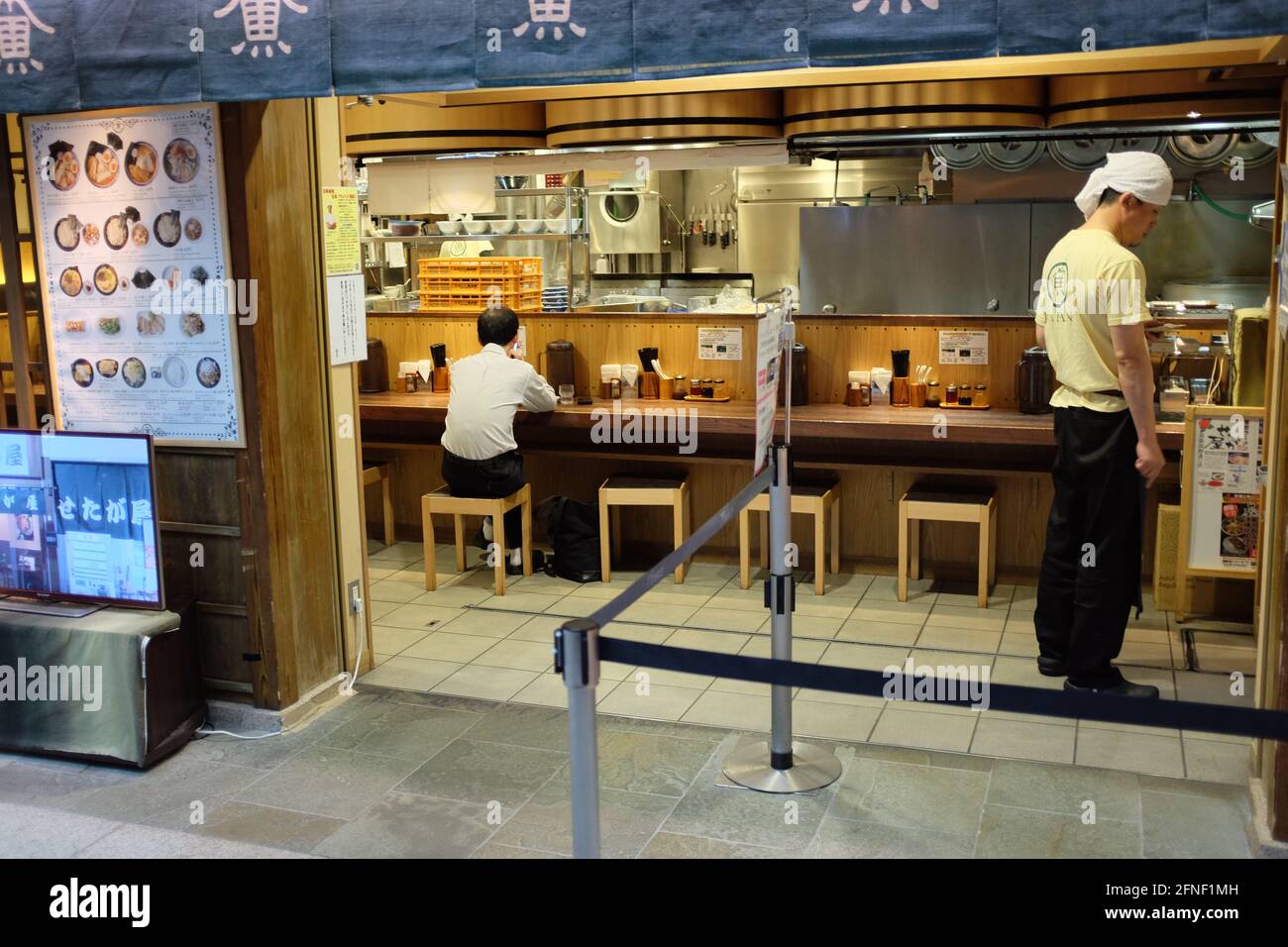 A Japanese business man sits at a Sushi bar restaurant while an employee attends the counter in Toykyo, Japan Stock Photo