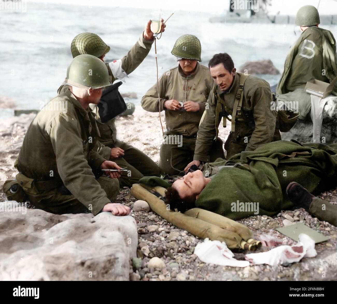 A captain and medics treated a wounded soldier of the 1st US Infantry Division at Omaha Beach, France. The soldier was wrapped in an army blanket whil Stock Photo