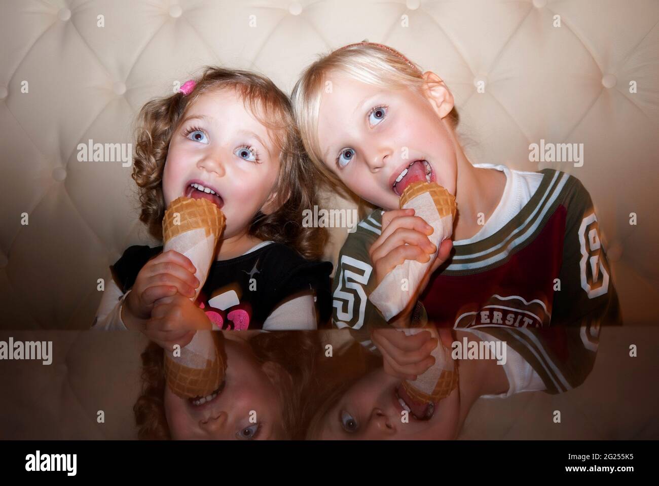 Two girls sitting on a sofa eating ice cream cones Stock Photo