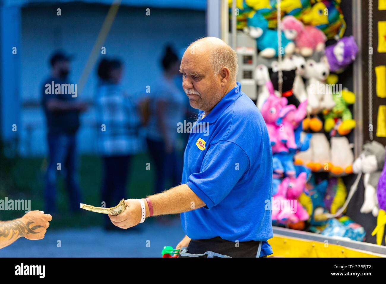 A worker exchanges money with a player in a carnival game at the 2021 Noble County Fair in Kendallville, Indiana, USA. Stock Photo