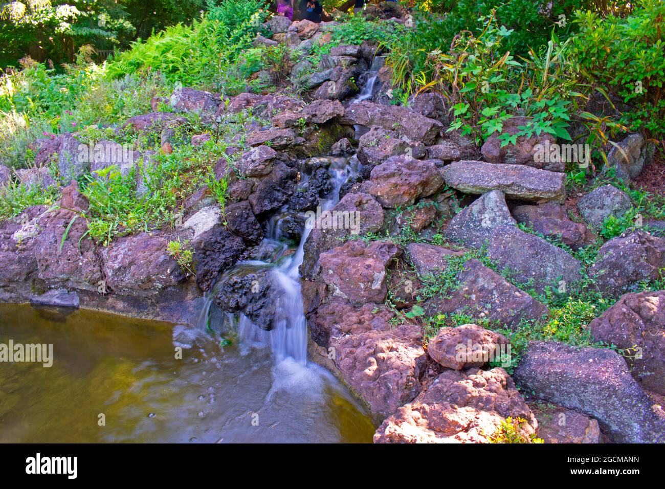 Long exposure shot of a small, man-made waterfall and rock garden in a local park Stock Photo