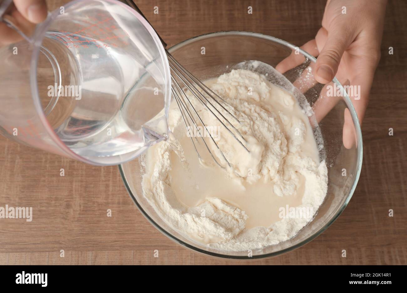 Pouring water into glass bowl with flour on table Stock Photo