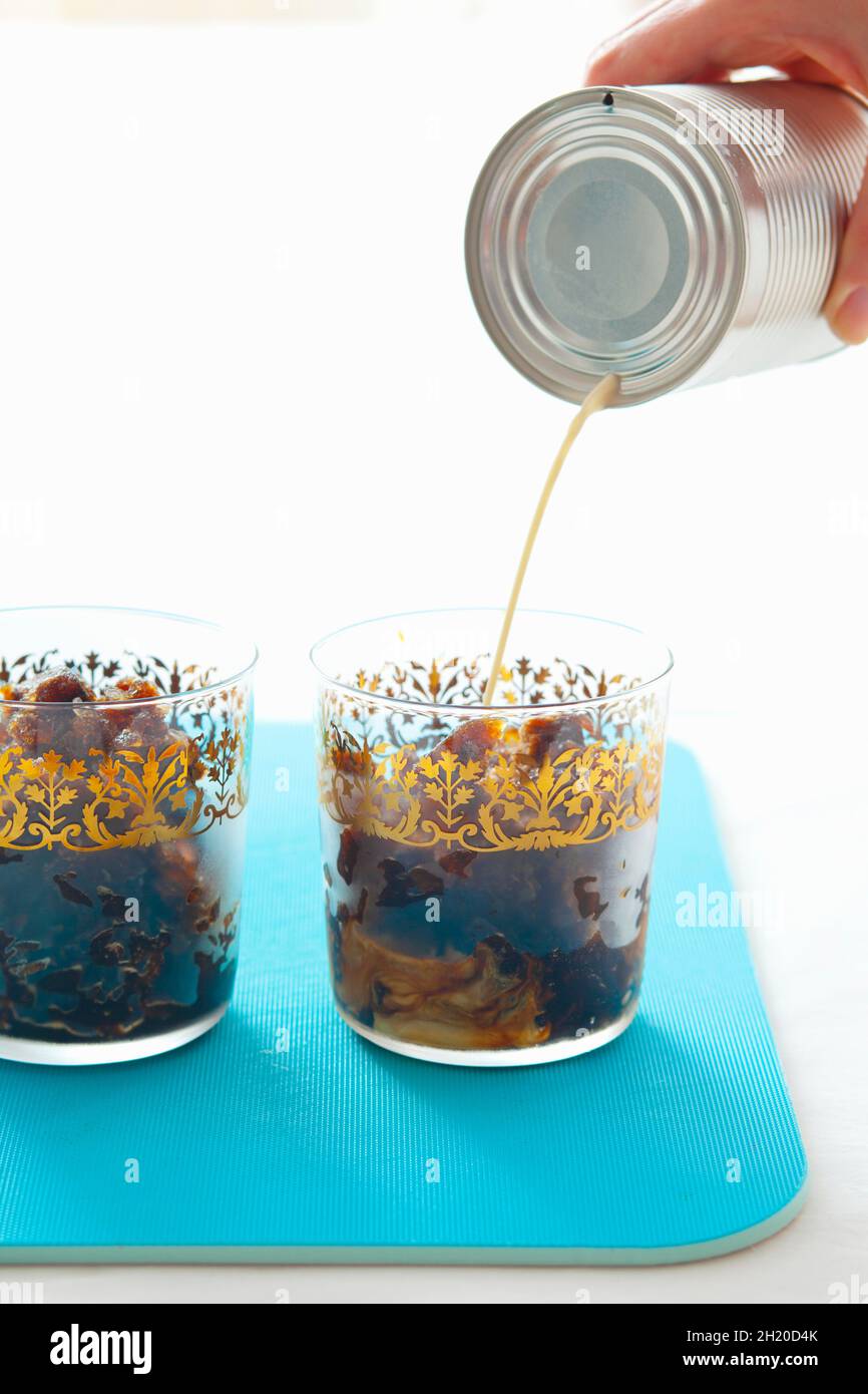 Condensed milk being poured into iced coffee Stock Photo