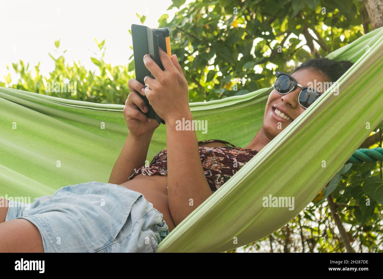 Beautiful dark-skinned woman reads in a hammock by the ocean Stock Photo