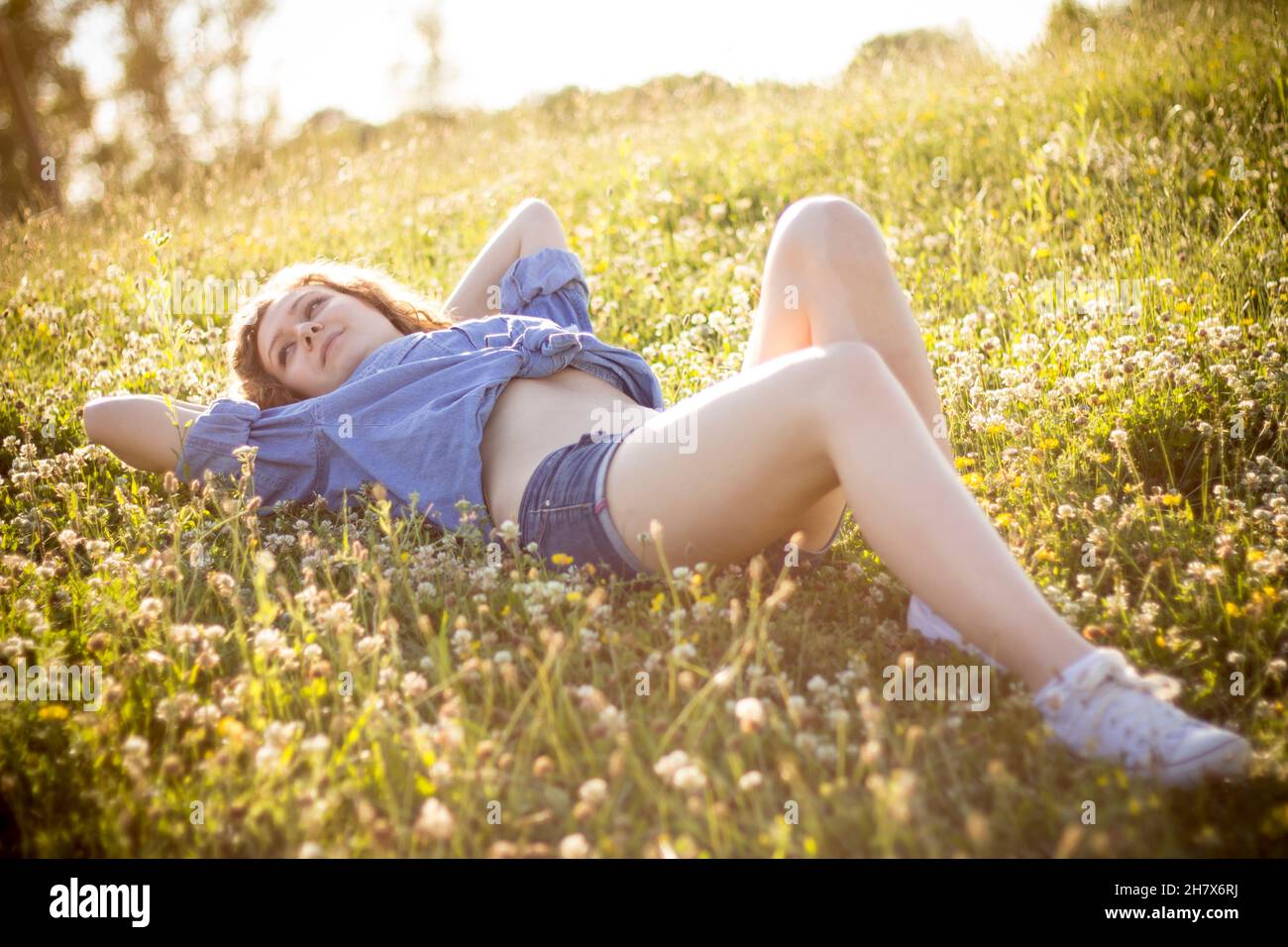 Young blonde countrygirl in denim buttoned shirt wearing hot jean shorts posing in summer golden hour outdoors seductively looking at camera Stock Photo