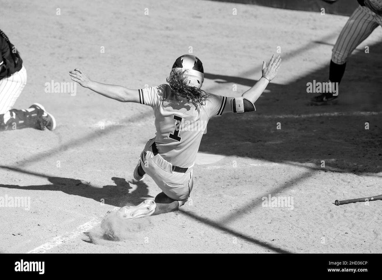 A Baseball Player Is Sliding Into Home Plate To Beat the Throw Home And Score A Run In A Black And White Image Stock Photo