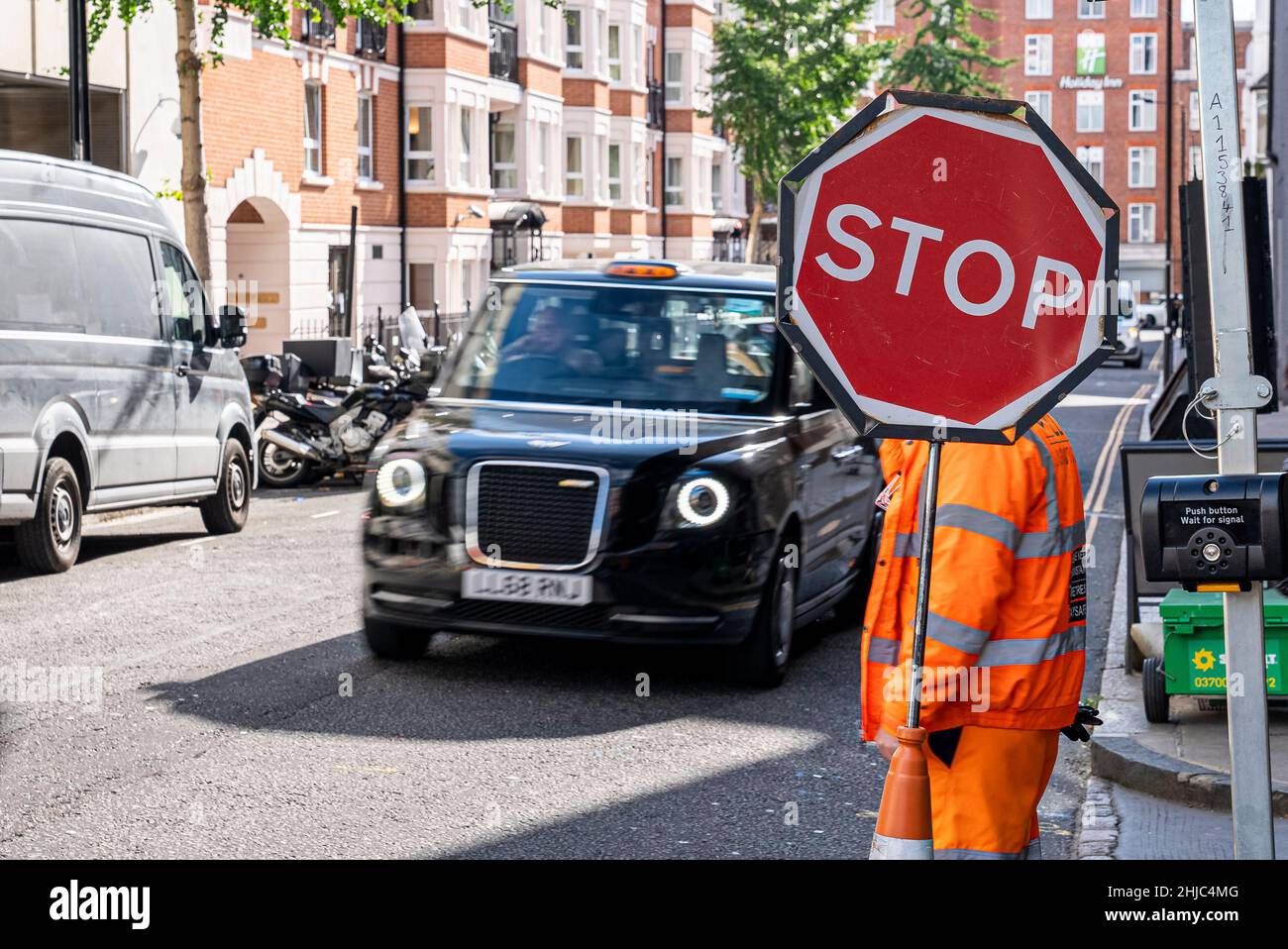 Urban city road traffic with stop sign and worker in coveralls at sidewalk Stock Photo