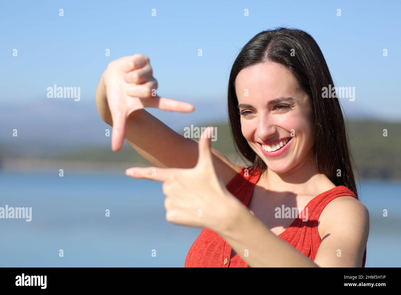 Happy woman in red framing gesturing with hands in a lake on vacation Stock Photo