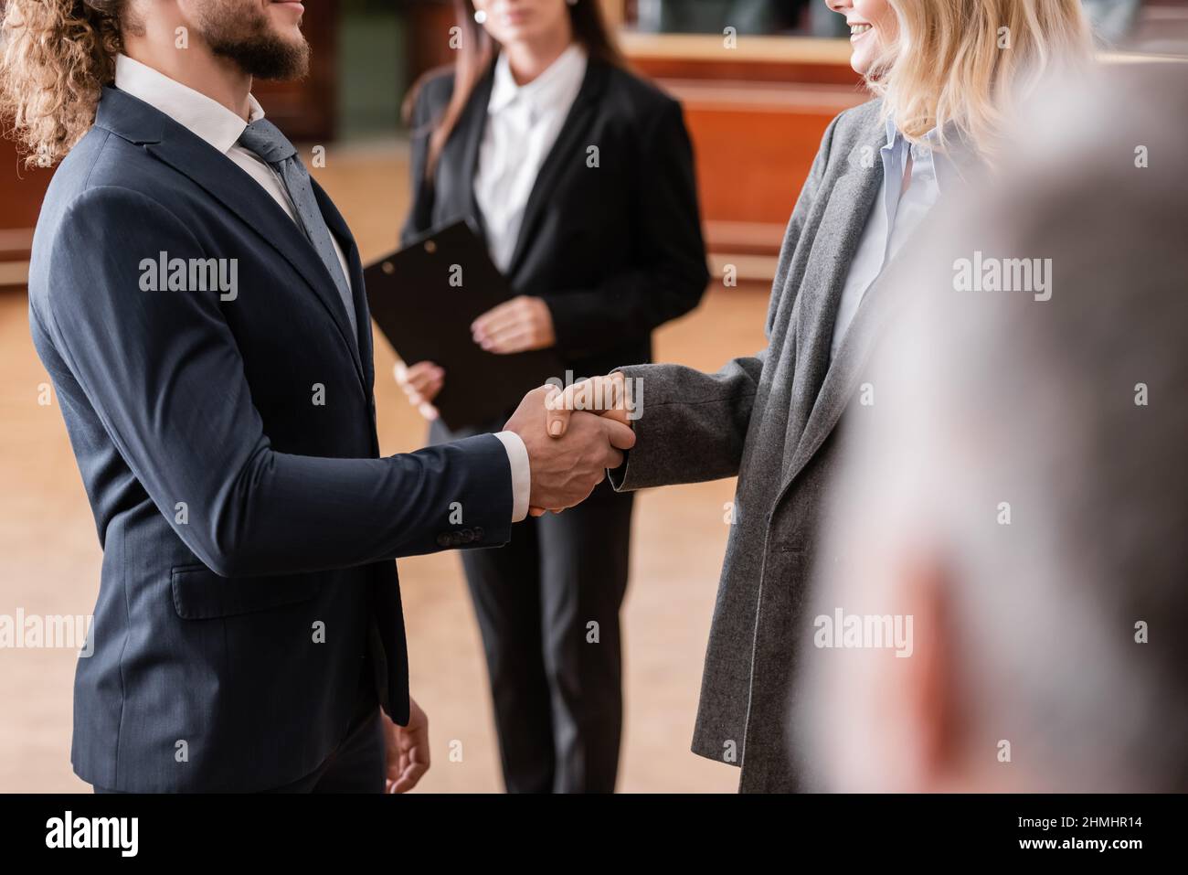 partial view of justified businessman shaking hands with smiling advocate in court Stock Photo