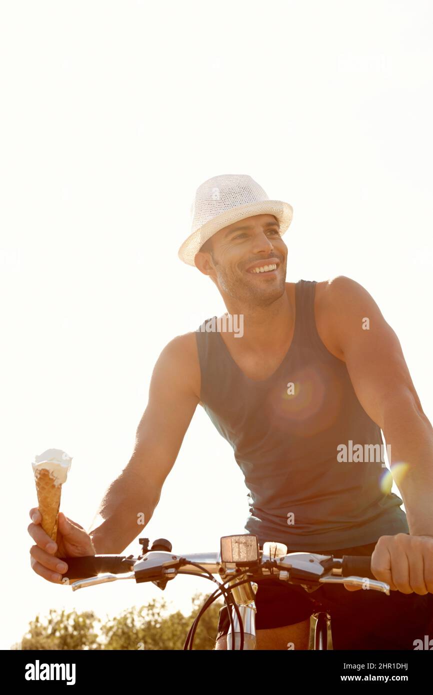 Enjoying an ice-cream cone and a bike ride. Shot of a handsome young man eating an ice-cream while riding his bicycle outdoors. Stock Photo