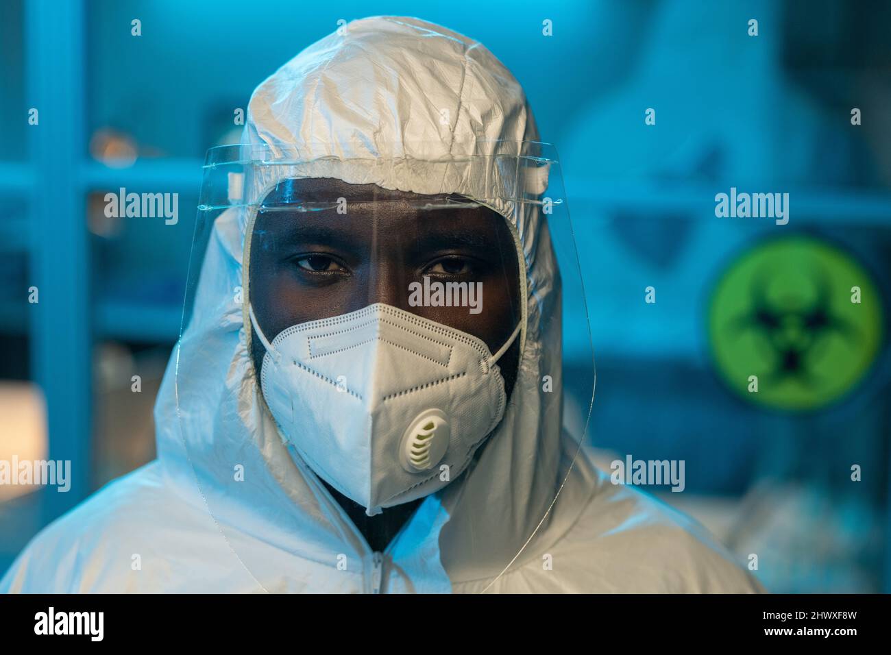 Shot of young contemporary African American scientist in coveralls, protective screen on face and respirator looking at camera Stock Photo