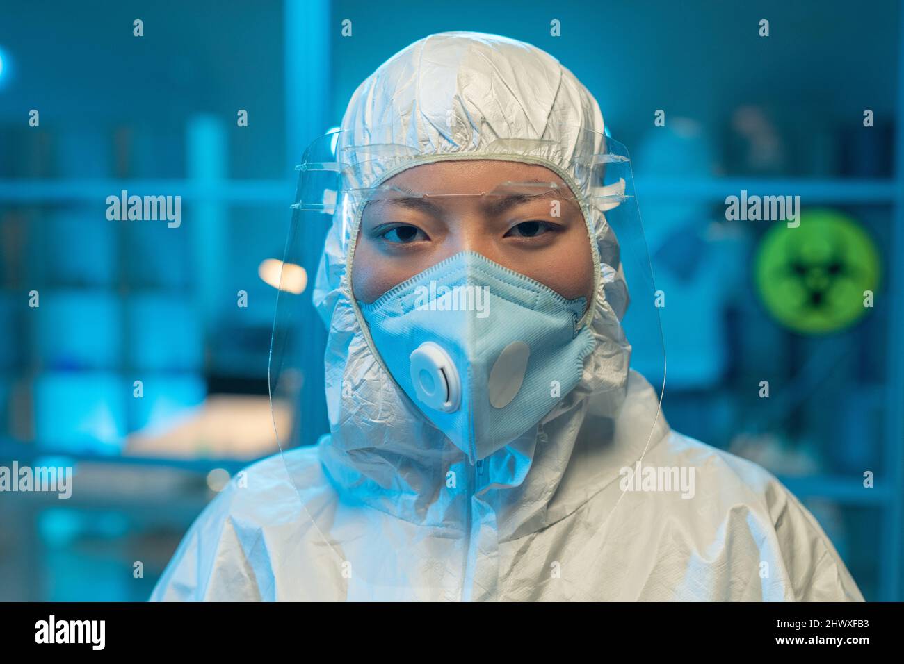 Young Asian female microbiologist or clinician in protective coveralls looking at camera in modern scientific laboratory Stock Photo