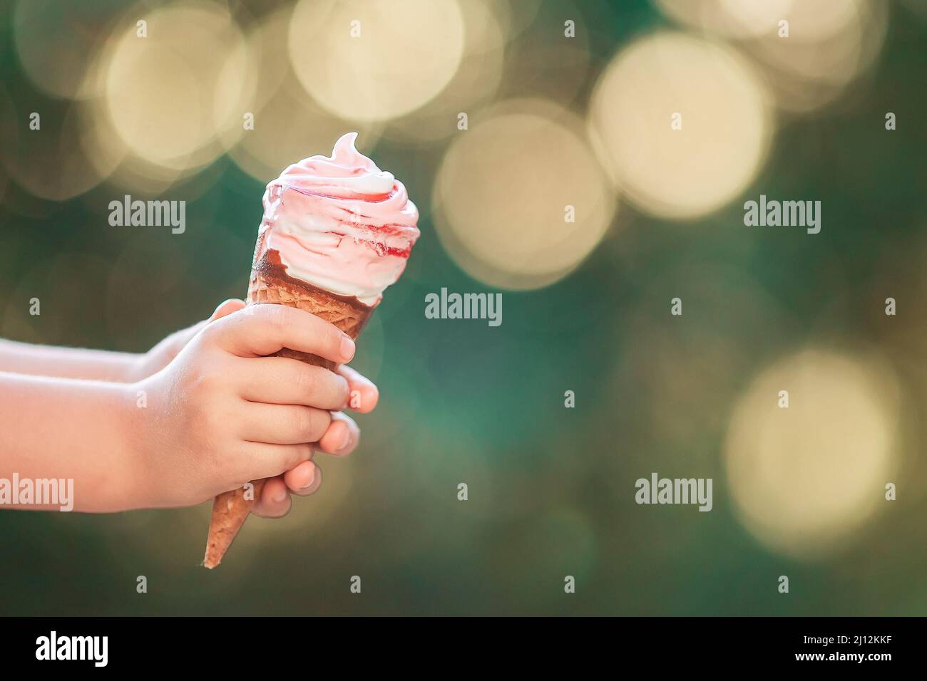 Baby toddler hand holding a large strawberry ice cream in a waffle cone on a bokeh background Stock Photo