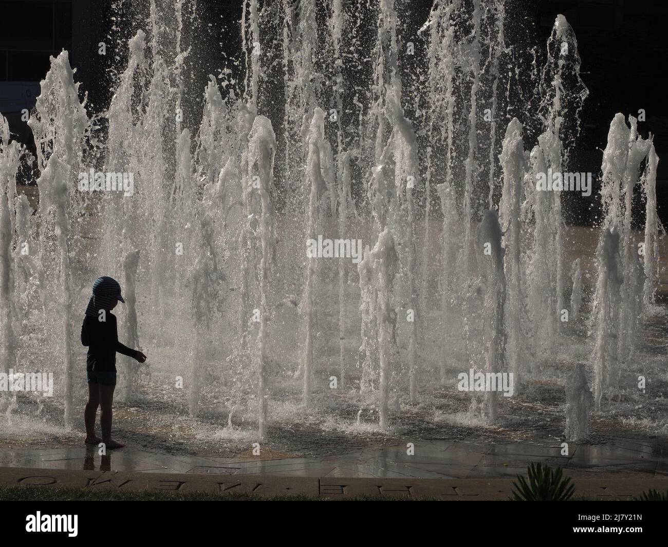 anonymous small child in backlit silhouette contrasts with frothing white city centre ornamental feature fountains - Sheffield, Yorkshire, England, UK Stock Photo