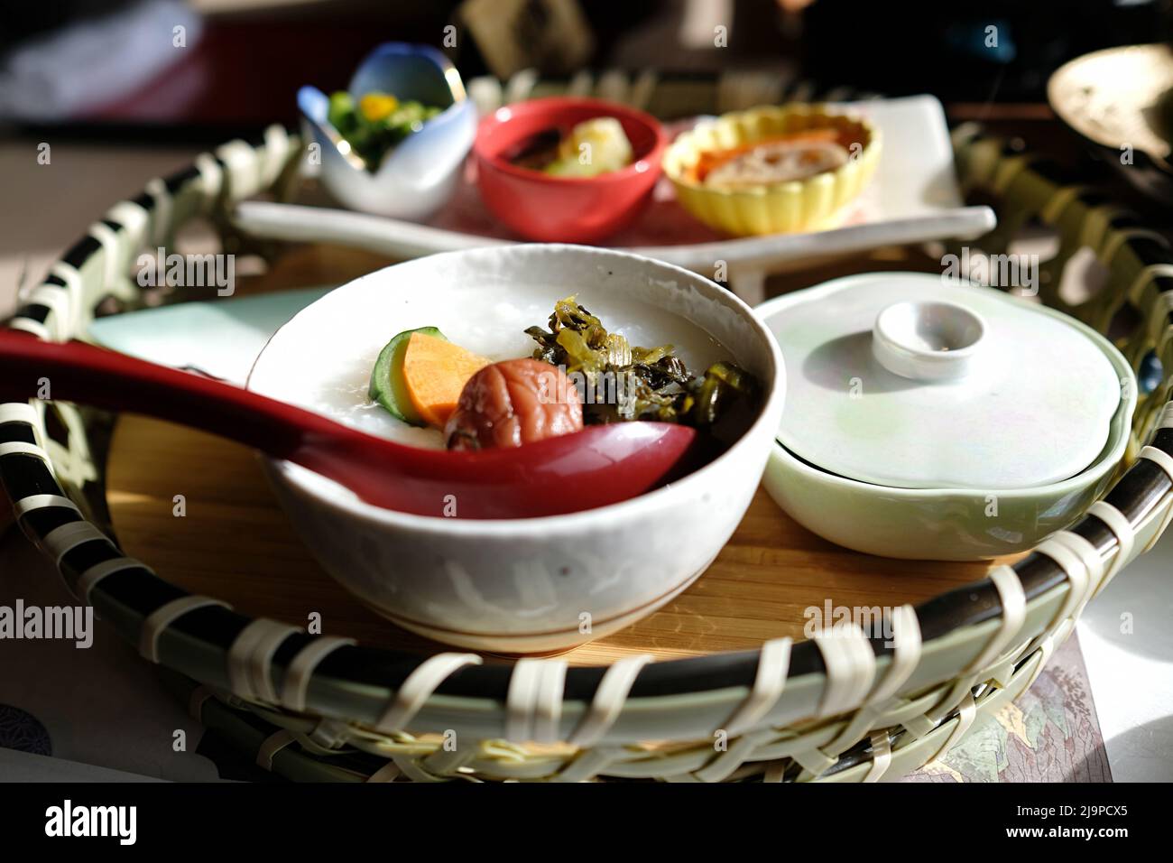 Rice porridge with umeboshi, pickles and steamed vegetables, and an assortment of side dishes: lotus root, edamame, etc Stock Photo