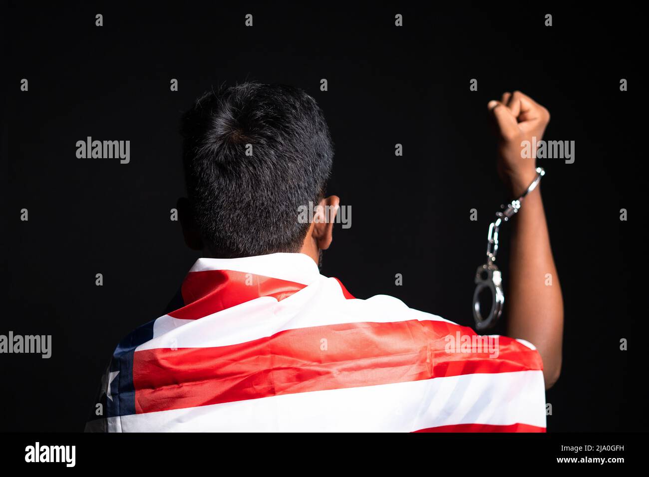 back view shot of man with us or american flag on shoulder showing hands with released cuffs on black background Stock Photo