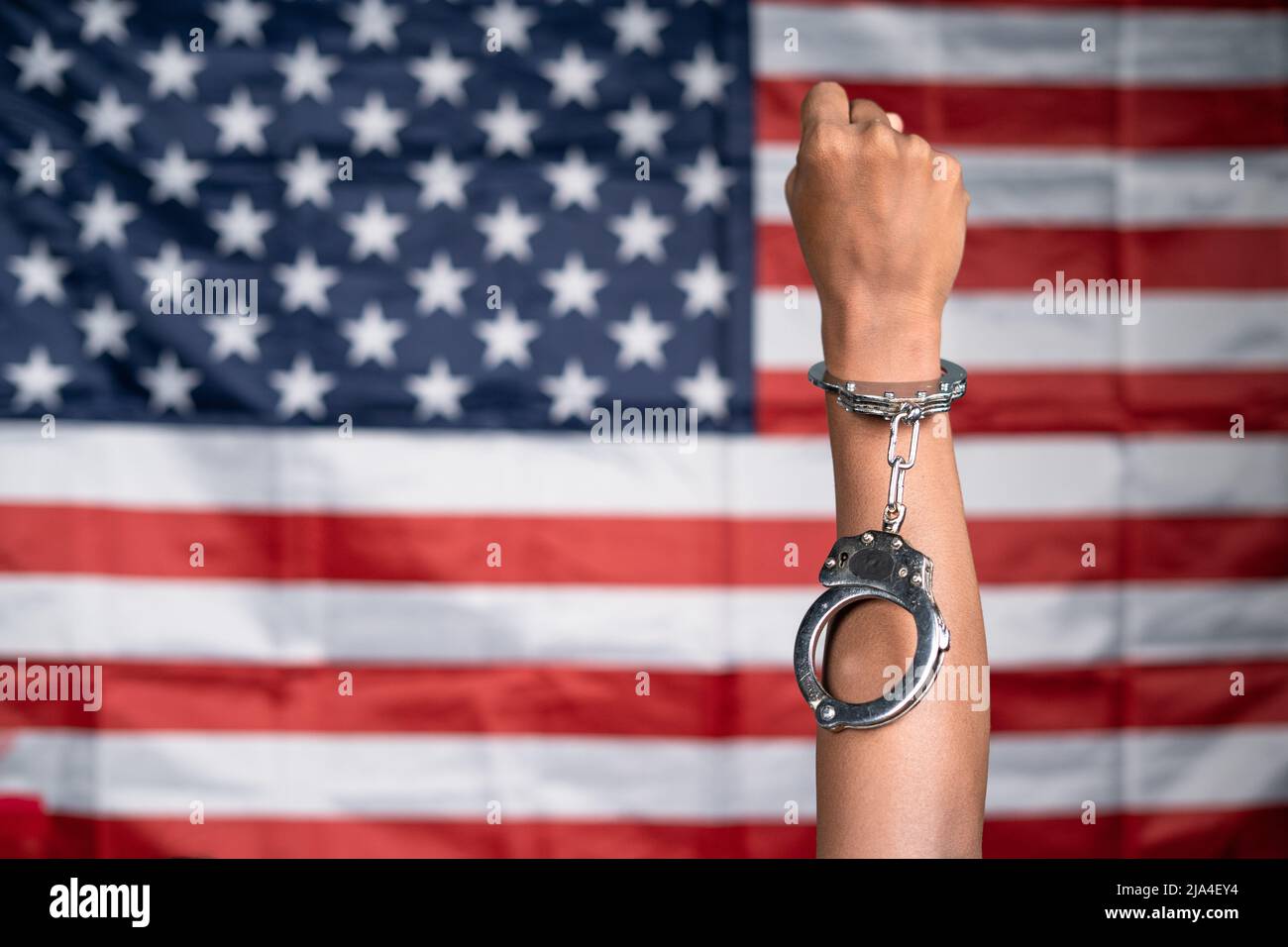 Close up shot of hanads rising with released cuffs against us or american flag as background - concept of juneteenth, freedom and justice. Stock Photo