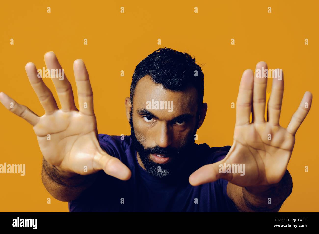 closeup portrait of a handsome young adult man with a beard and a mustache hands framing camera fingers pointing on a yellow background studio Stock Photo