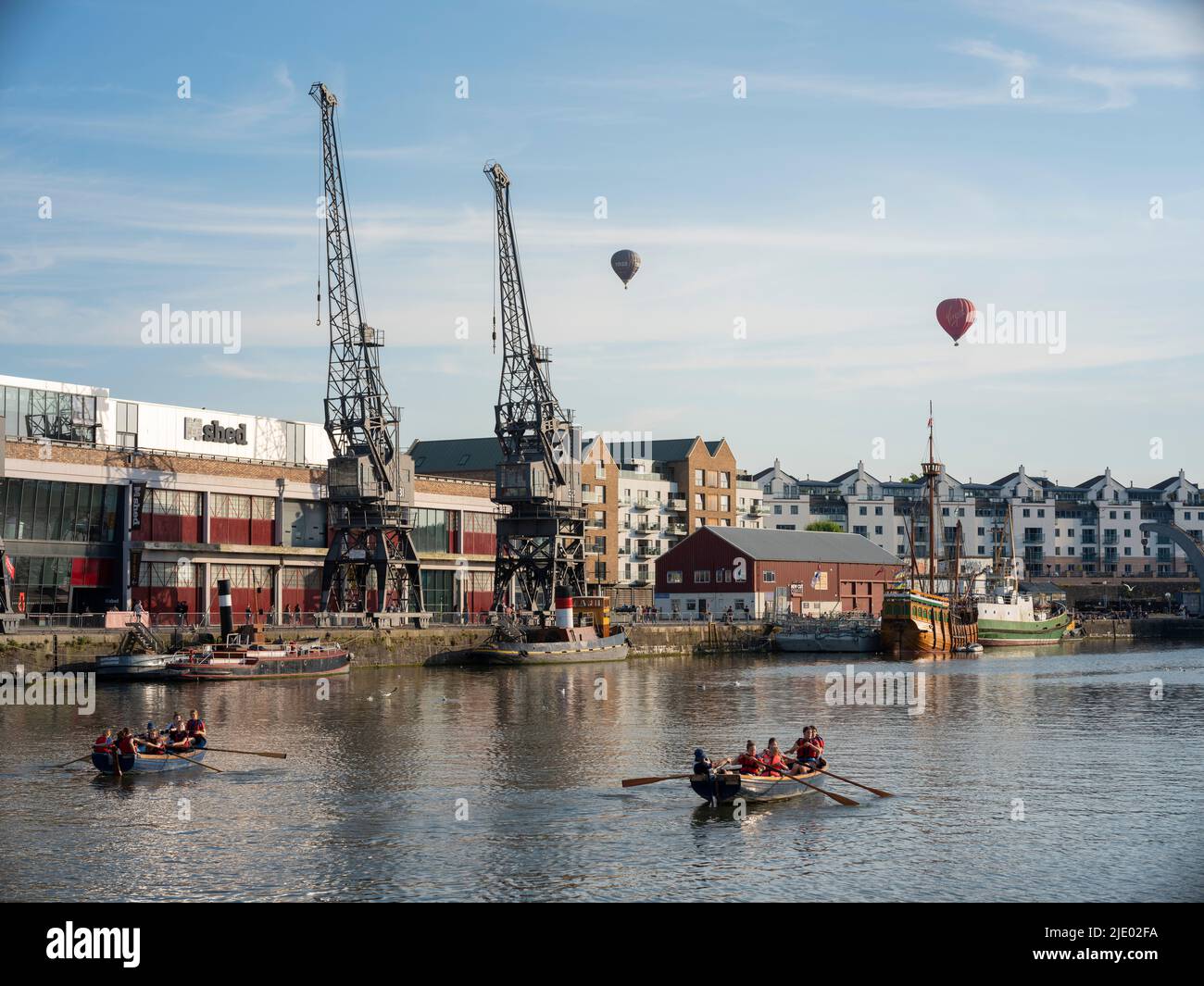 Hot air balloons float over the cranes, rowing boats, and the mShed in the floating harbour harbourside area of Bristol on a sunny summer evening. Stock Photo