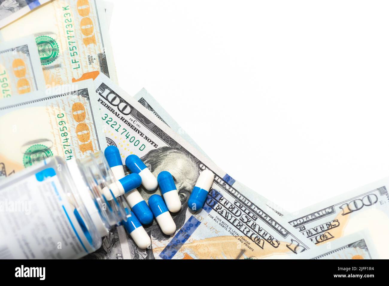 Capsule pills white-blue close-up scattered on 100 dollar American bills with a white background for writing. Stock Photo