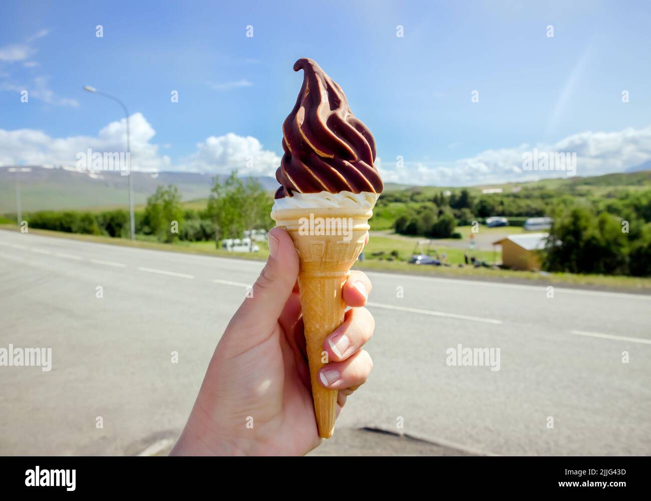 Hand holding tasty Icelandic local soft serve vanilla ice cream dipped in hot chocolate, Iceland nature on background. Stock Photo