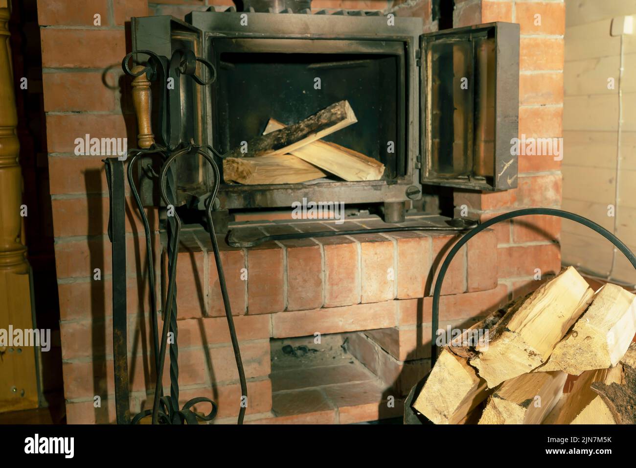 open doors of a cast-iron fireplace insert and firewood stacked inside Stock Photo