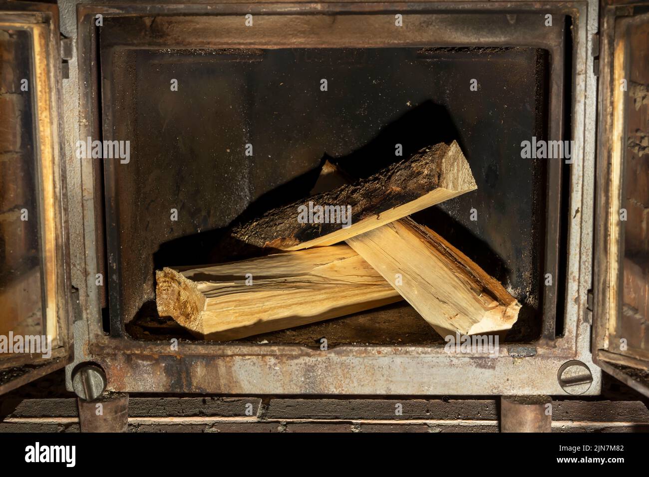 open doors of a cast-iron fireplace insert and firewood stacked inside Stock Photo