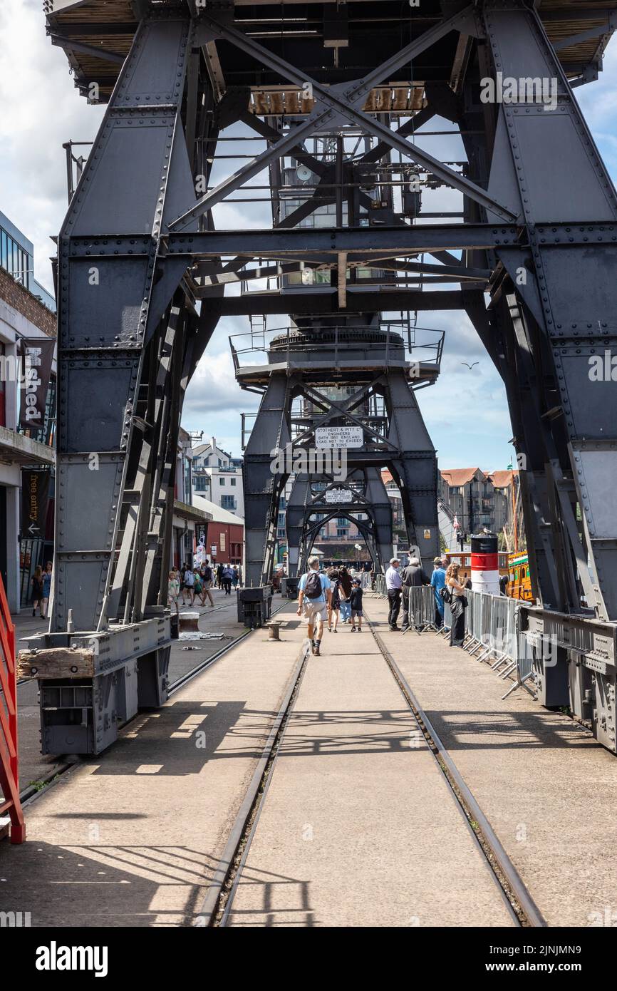 The M Shed’s electric cargo cranes with people walking underneath, Bristol Docks, Bristol harbourside - floating harbour, City of Bristol, England, UK Stock Photo