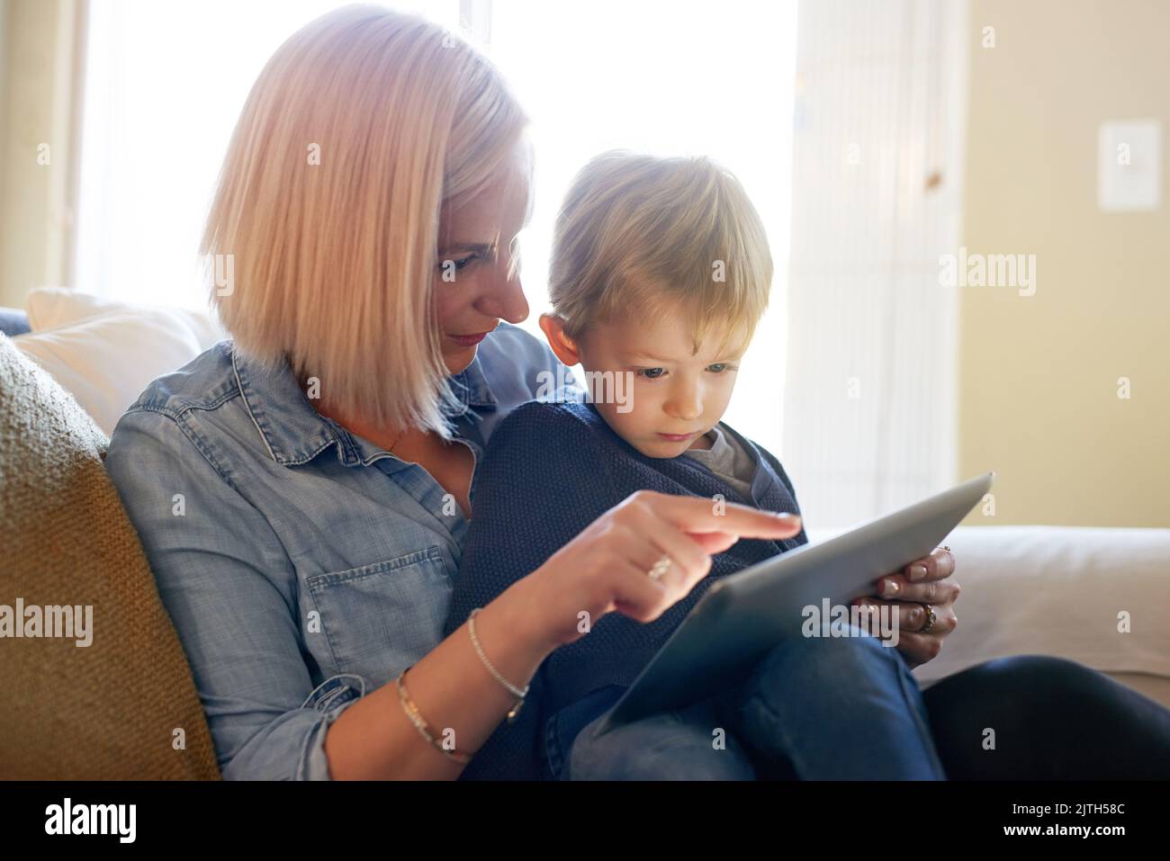 Moms downloaded him a safe new app to play on. a mother and son using a digital tablet together at home. Stock Photo