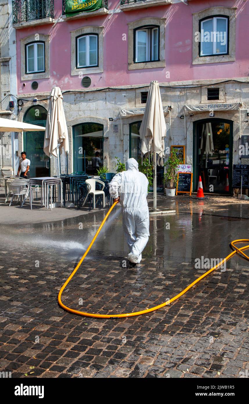 Full PPE white protective disposable suit Street cleaning with hose pipe in Lisbon Portugal Stock Photo