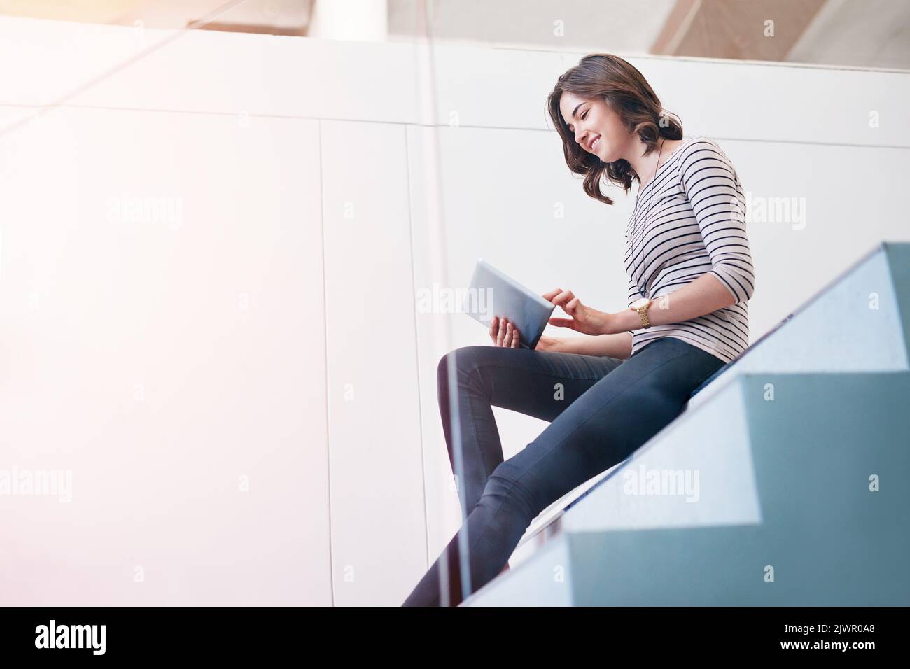 Loading her tablet with apps for her business. a young businesswoman using a digital tablet on the stairs in a modern office. Stock Photo