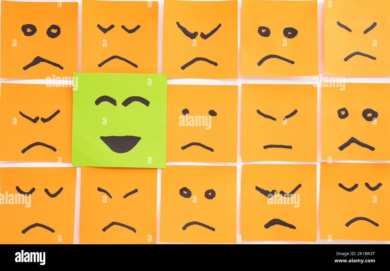 Concept for a positive attitude made with papers looking like sad faces with one that has smile and stands out Stock Photo