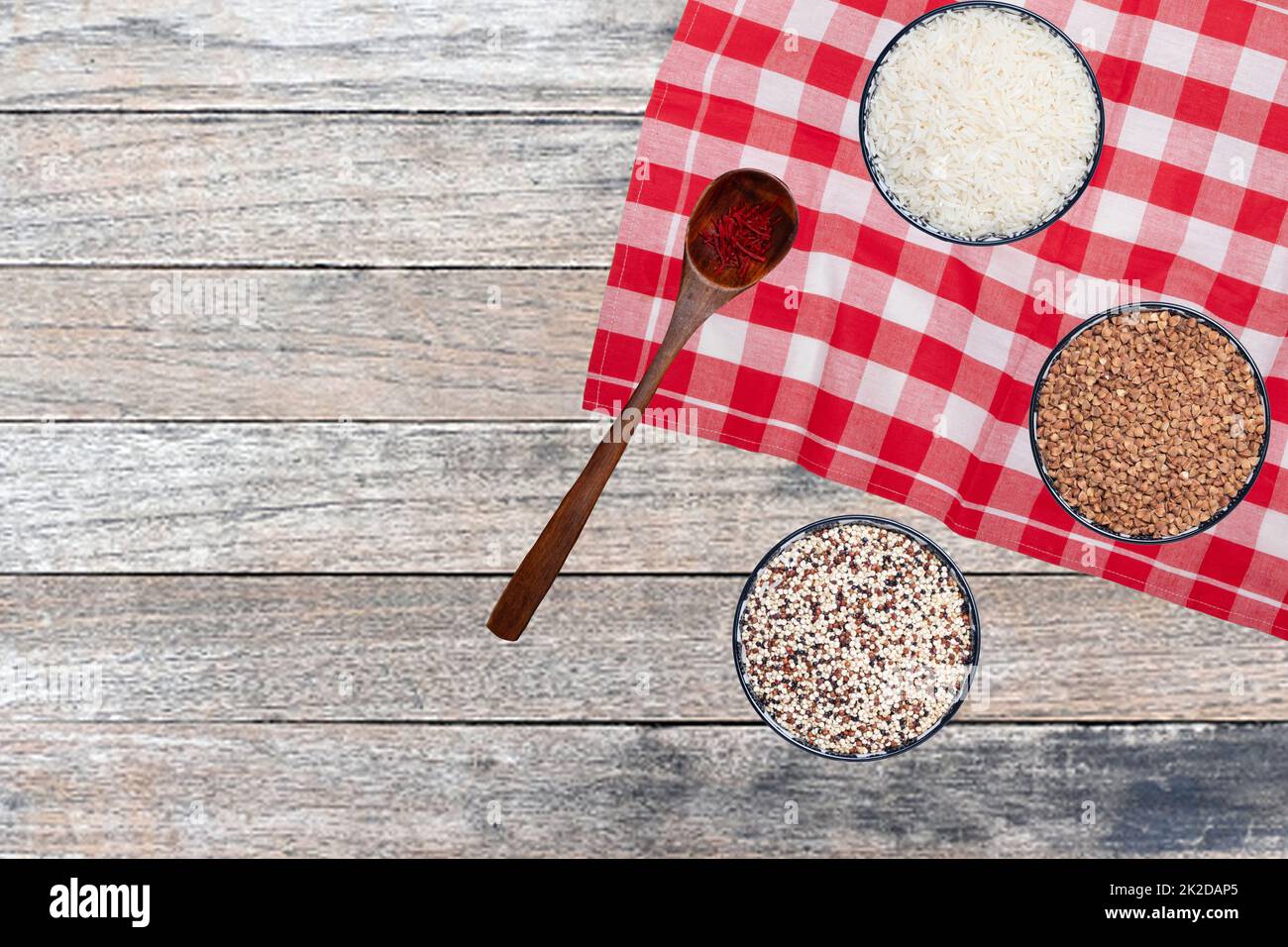 Vegetable food. Closeup of three bowls with rice, buckwheat and quinoa and a spoon with safran spice threads on abstract blurred table. Healthy eating.Top view with space. Stock Photo