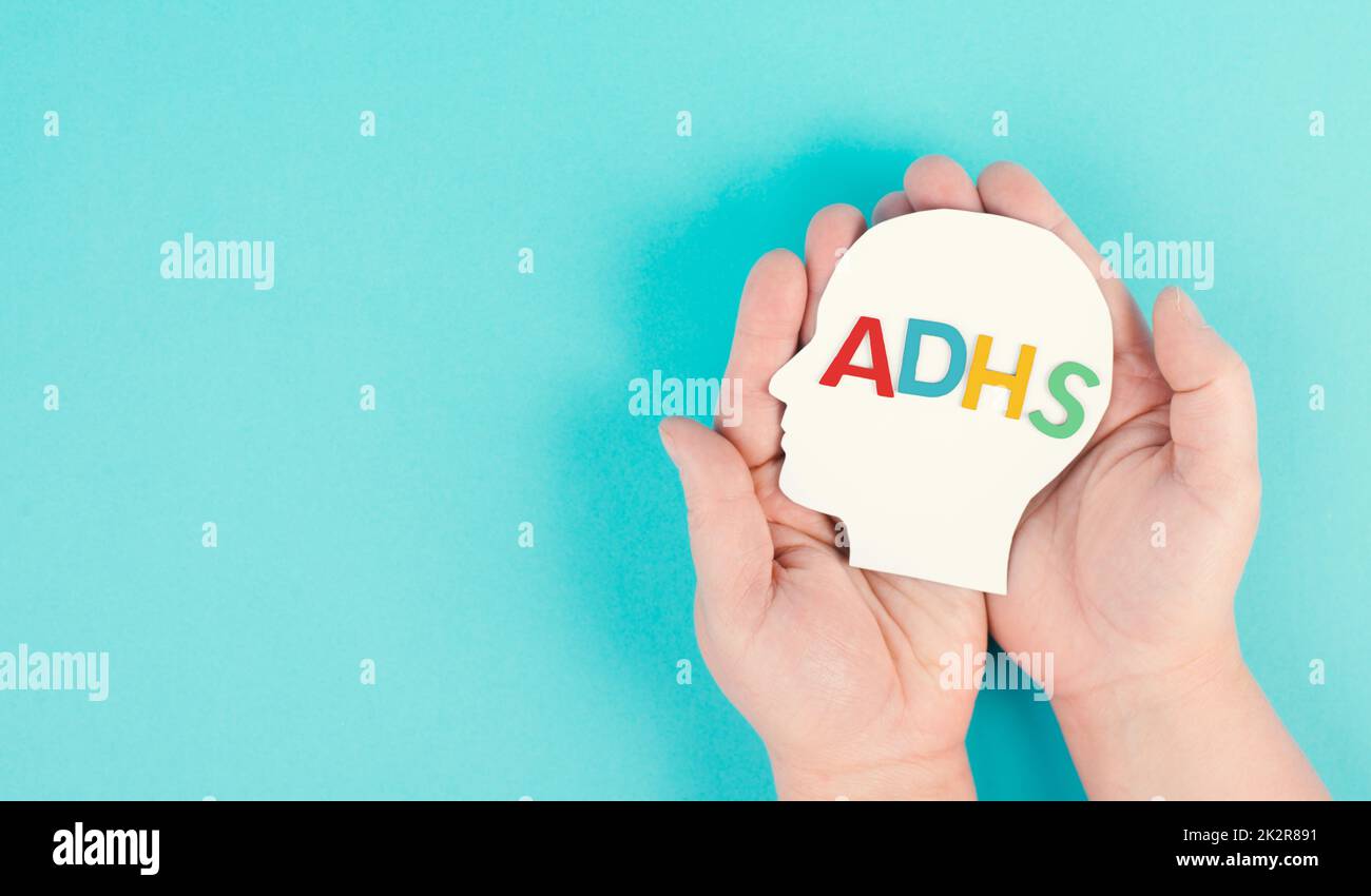 Hands holding a head with the german word ADHS which means attention deficit hyperactivity disorder, ADHD symptom, mental health Stock Photo