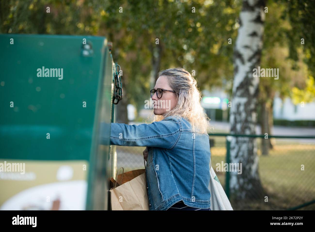 Blond woman throwing rubbish into waste bin Stock Photo