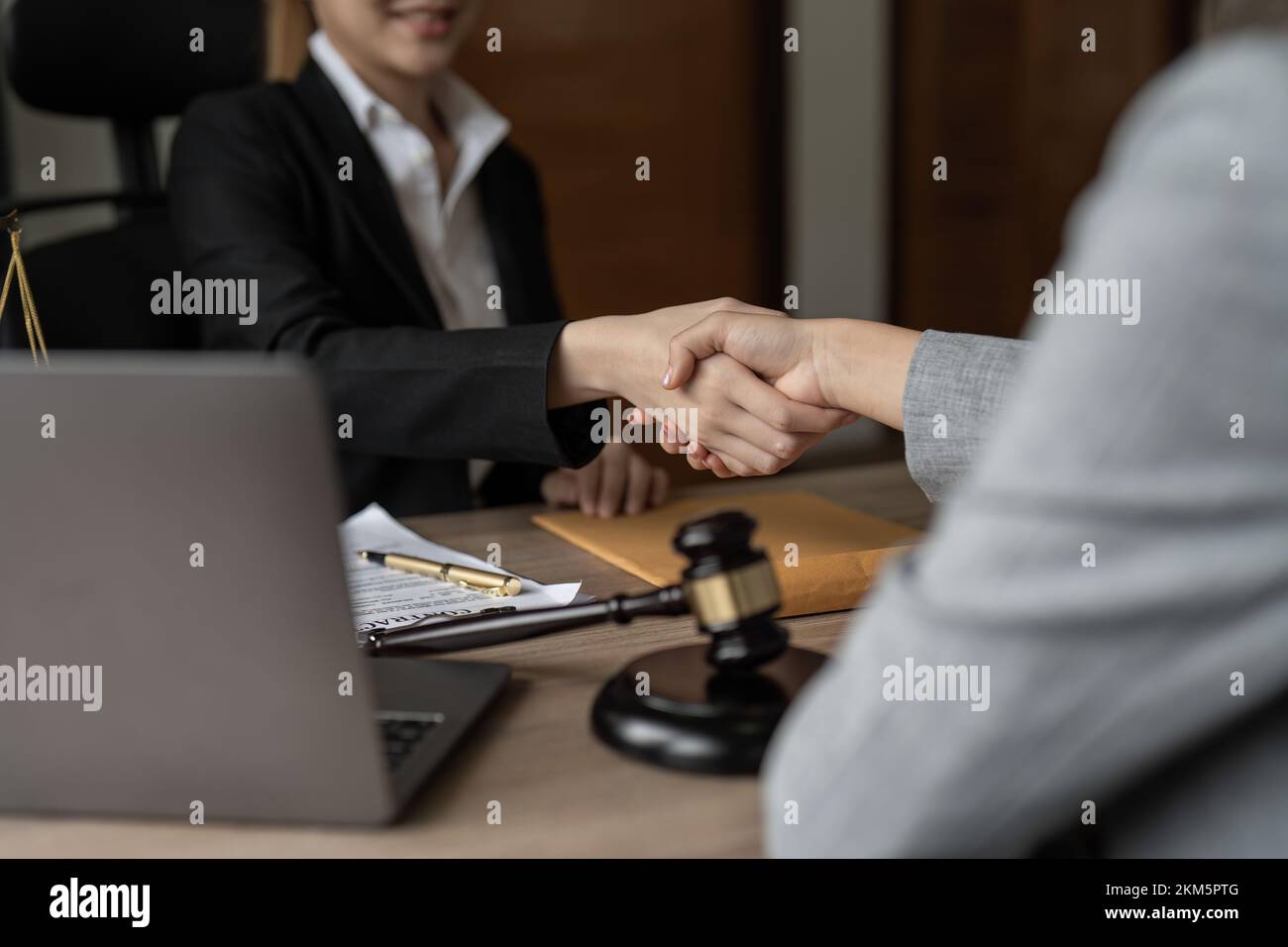 Gavel Justice hammer on wooden table with judge and client shaking hands after adviced in background at courtroom, lawyer service concept. Stock Photo