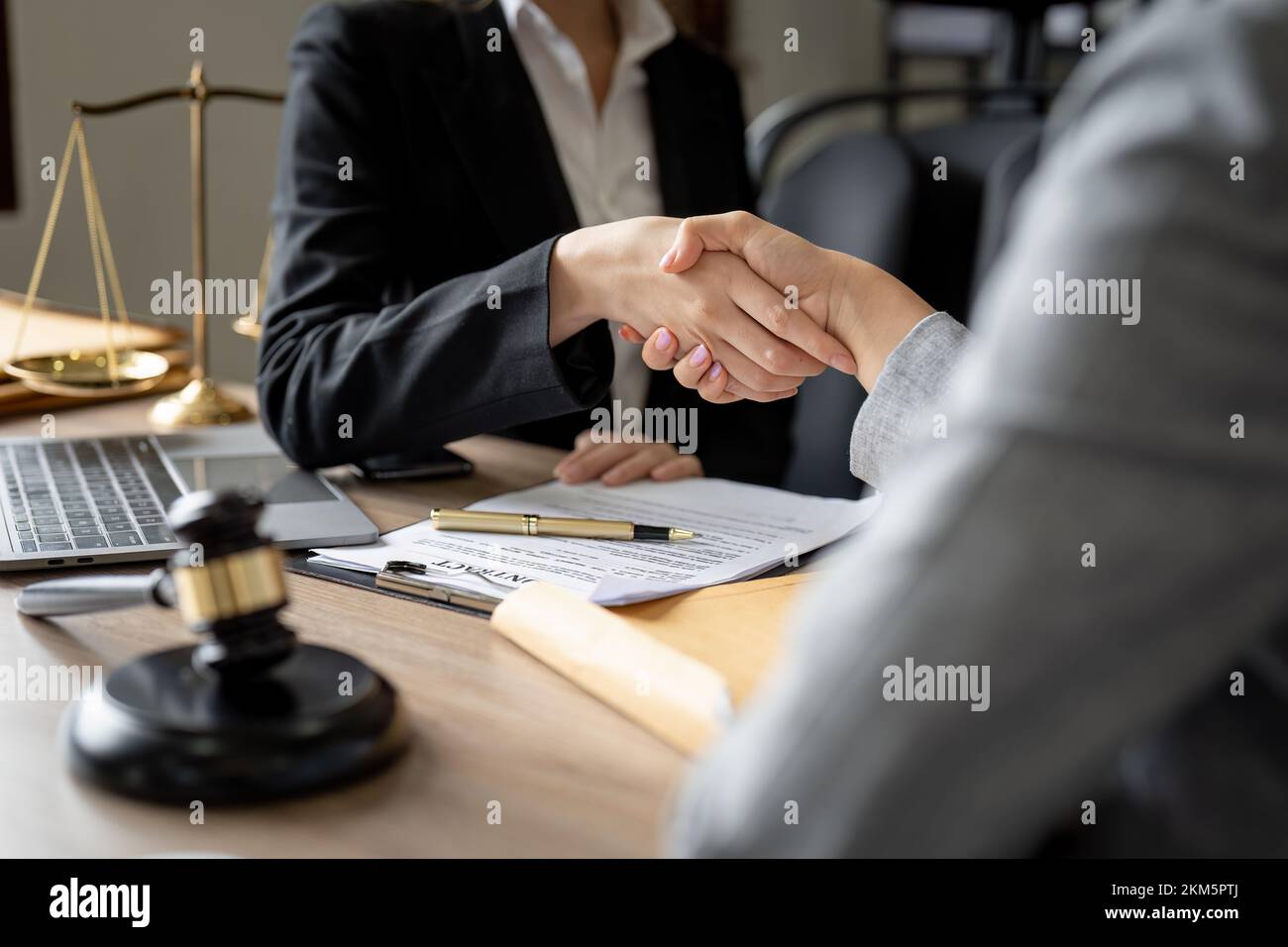 Gavel Justice hammer on wooden table with judge and client shaking hands after adviced in background at courtroom, lawyer service concept. Stock Photo